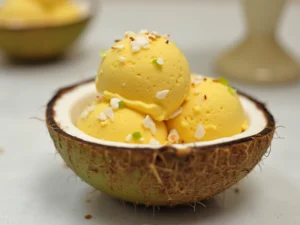 Tropisches Mango-Kokos-Eis, serviert in einer Kokosnussschale mit Kokosraspeln und Limettenzesten – eine exotische Kreation aus den Ninja Creami Rezepte.