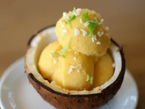 Exotisches Mango-Kokos-Eis, serviert in einer dekorativen Kokosnussschale mit gerösteten Kokosflocken – ein Highlight aus den Ninja Creami Rezepte.