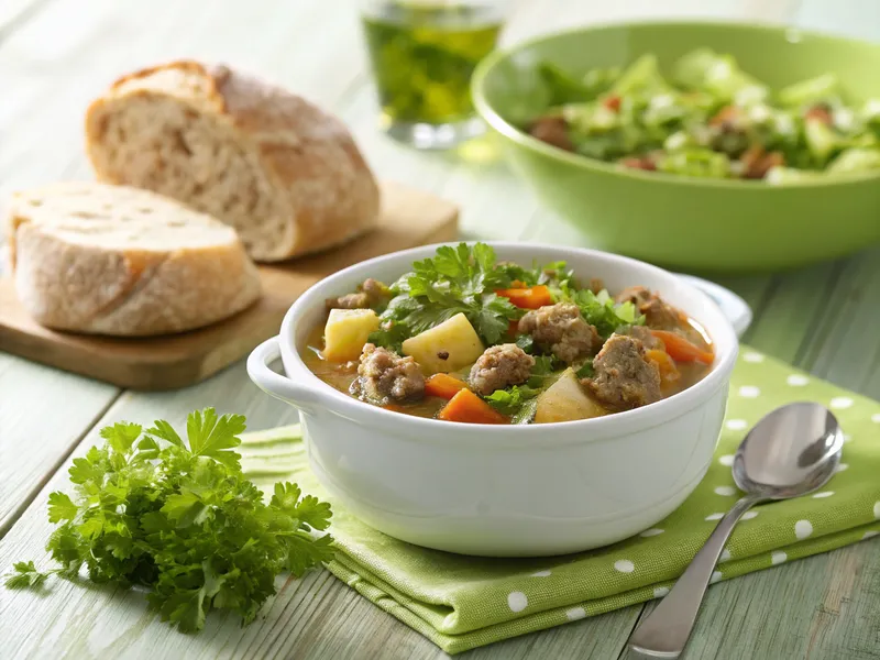 Hackfleisch Eintopf in einer rustikalen Schüssel, serviert mit Baguette und einem frischen Salat auf einem eleganten grünen Tischset.